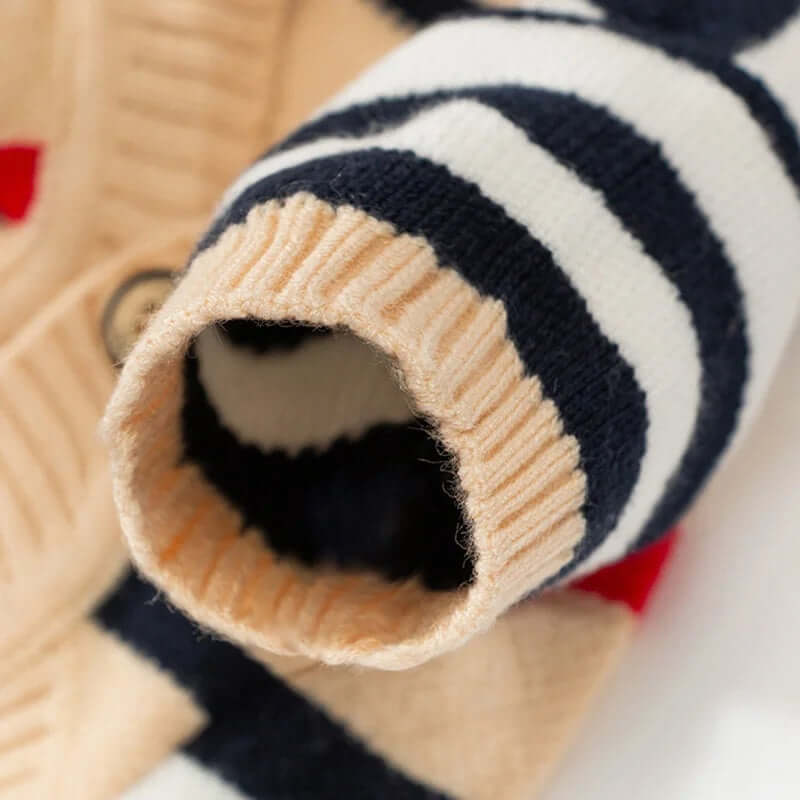 Close-up of the sleeve of a beige cardigan with black and white stripes, highlighting the ribbed cuff detail