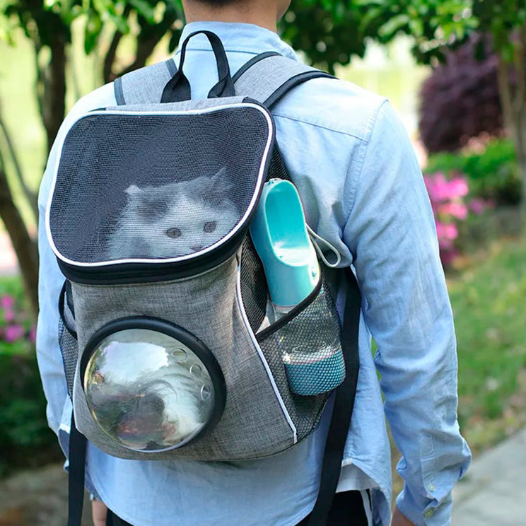 A person carrying a pet in a backpack with a PetPal Water & Snack Bottle bottle in a side pocket, showing outdoor usability.